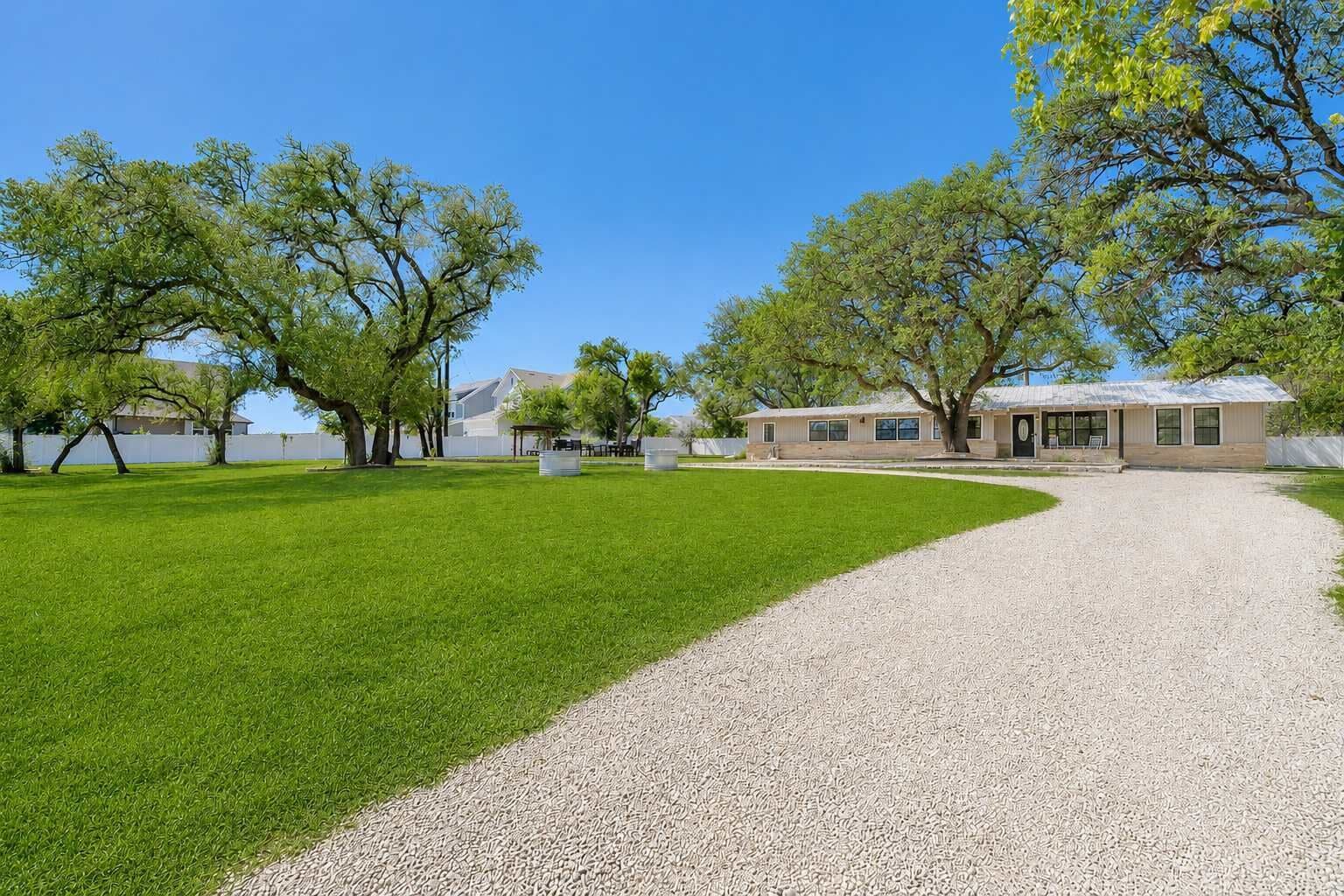 A residential property with a gravel driveway leading to a house, surrounded by a well-maintained lawn and trees.