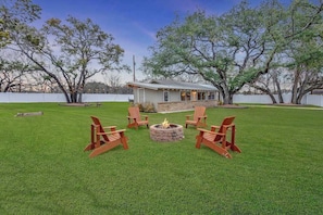 A backyard with a fire pit, four Adirondack chairs, and a house in the background.