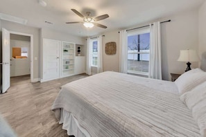 A bedroom with a bed, a ceiling fan, a window with curtains, and a door leading to another room.