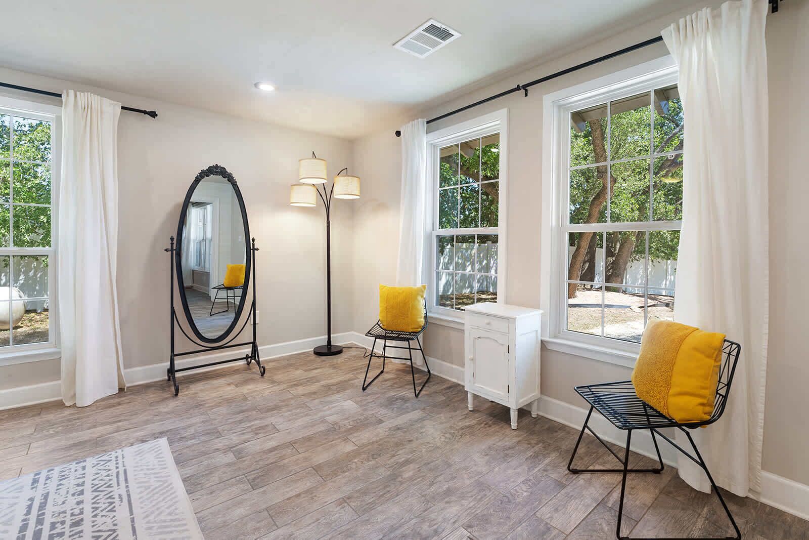 A room with a large mirror, two chairs with yellow cushions, a floor lamp, and a radiator.