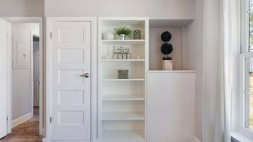 Un espace intérieur aux murs blancs, avec une porte, une bibliothèque intégrée et une fenêtre.