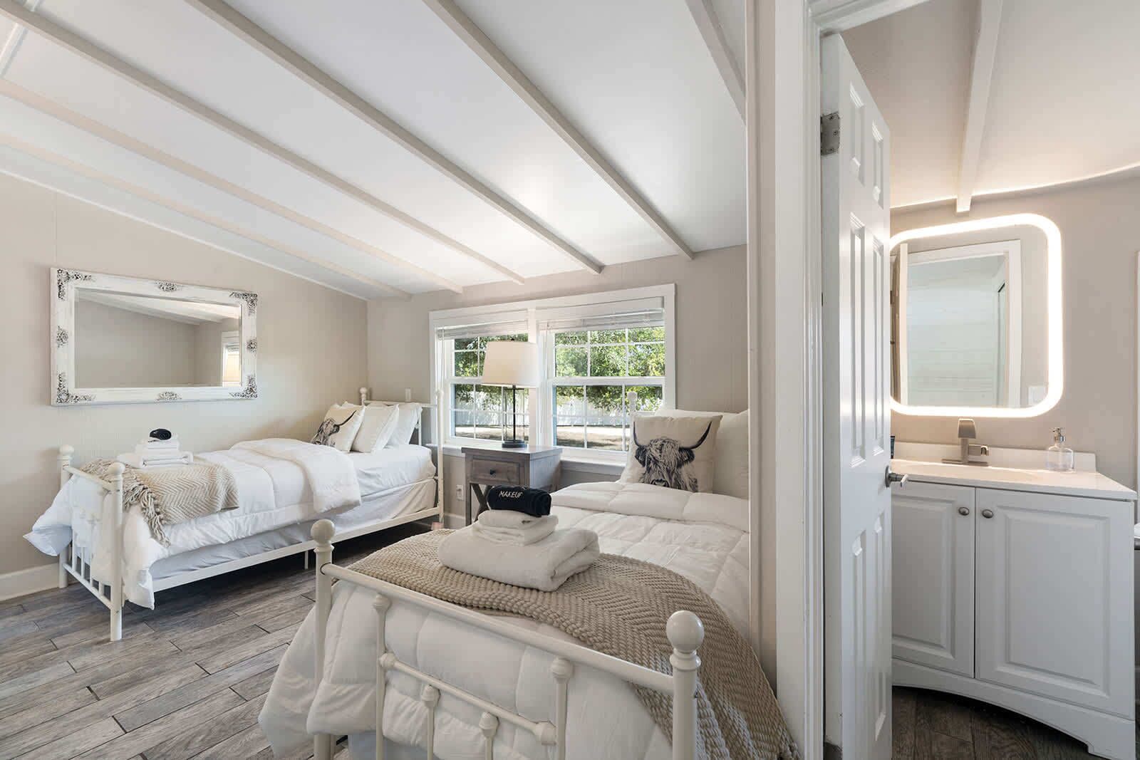 A bedroom with two beds, a window with a view, a bedside table, and a mirror.