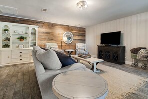 Ein Wohnzimmer mit einer Eckcouch, einem runden Couchtisch, einem Fernseher, einer Kommode mit Dekoration und einer Holz-Akzentwand.