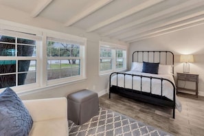 A bedroom with a bed, bedside table, lamp, and a view through large windows.
