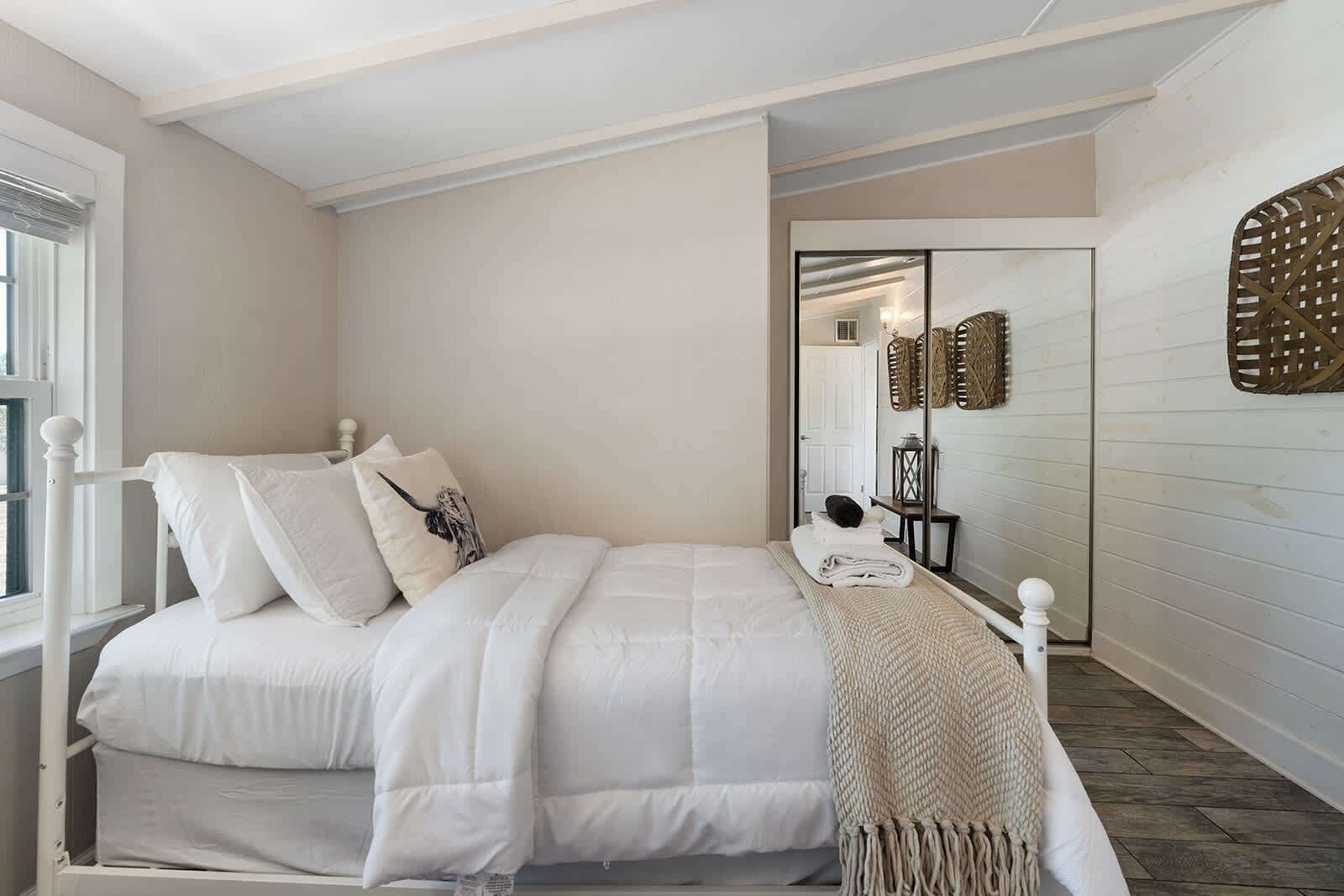 Un dormitorio con una cama, almohadas, una mesita de noche, un espejo y una puerta que da a otra habitación.