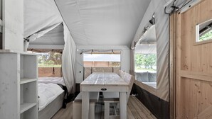 Una carpa con una mesa, bancos, suelo de madera y una ventana.
