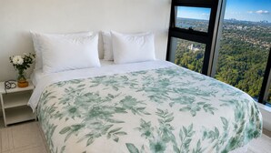 Ein Bett mit floralem Überwurf, weißen Kissen und Blick auf eine Stadtlandschaft durch ein Fenster.