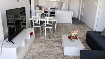 A modern living room with a flat-screen TV, a sofa, a coffee table with a vase, and a patterned rug.