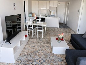 A modern living room with a flat-screen TV, a sofa, a coffee table with a vase, and a patterned rug. - Cozy apartment Sydney Olympic Park free parking 03 (Sydney Olympic Park)