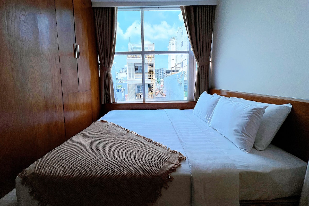 Ein Hotelzimmer mit einem großen Bett, einem Holzschrank und Blick auf Gebäude durch das Fenster.