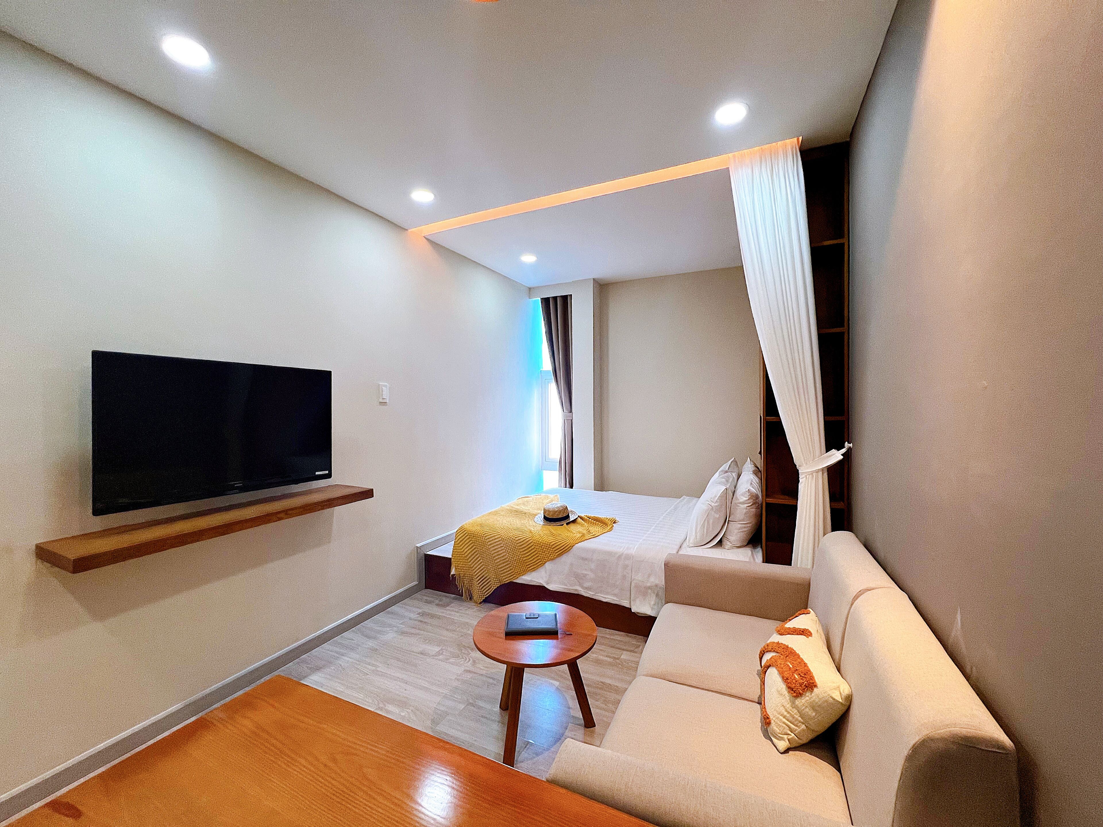 A modern hotel room with a flat-screen TV, a sofa, a small table, and a bed with a canopy.