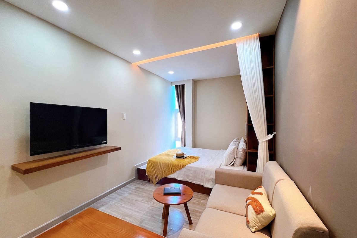 Ein modernes Hotelzimmer mit Flachbildfernseher, einer Couch, einem kleinen Tisch und einem Bett mit Baldachin.