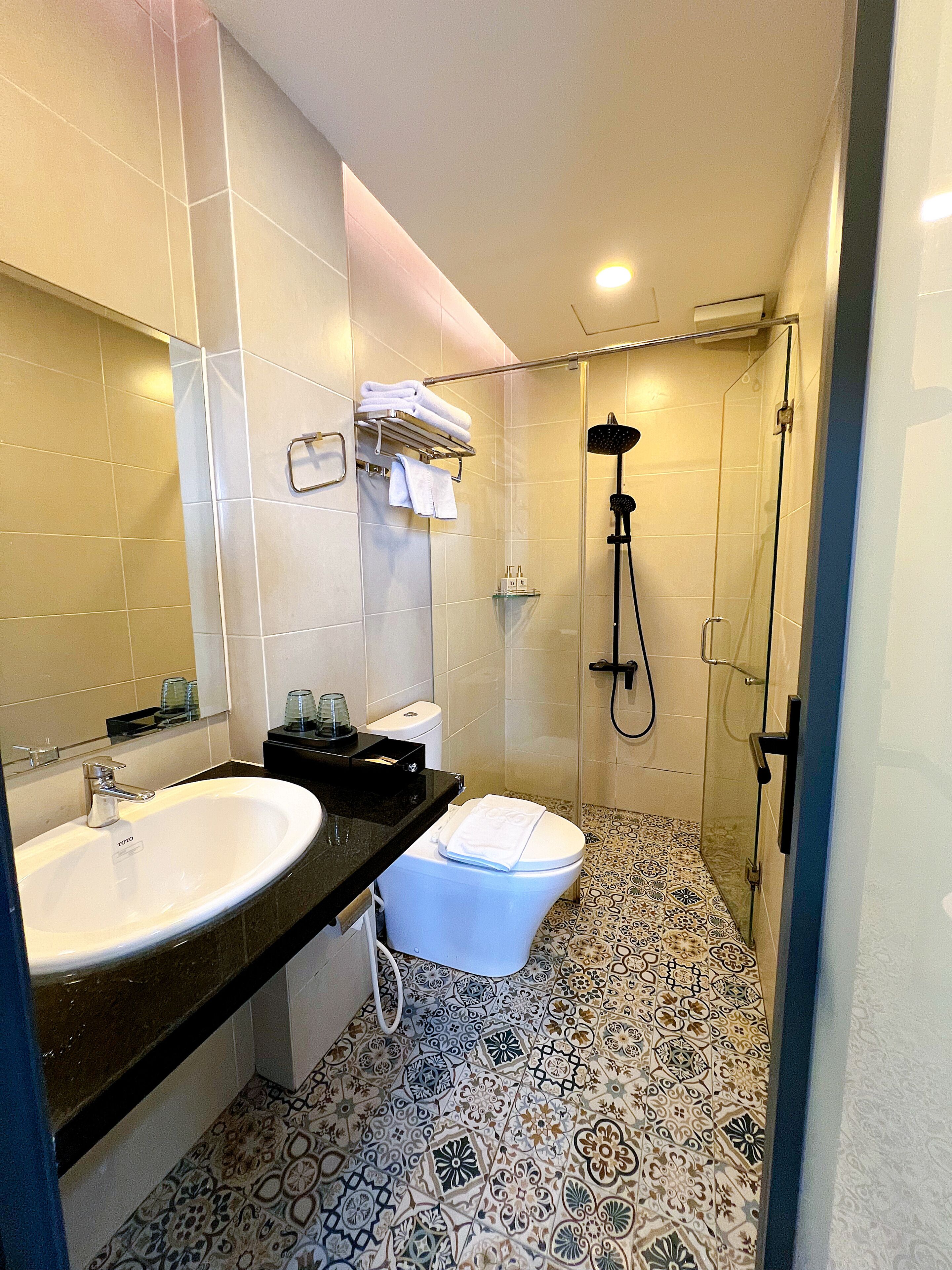 A bathroom with a sink, toilet, shower, and patterned floor tiles.
