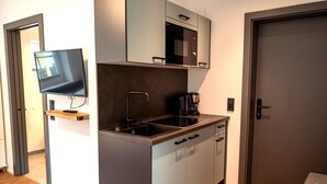 Een compacte keuken met een magnetron, fornuis en een flatscreen televisie aan de muur.