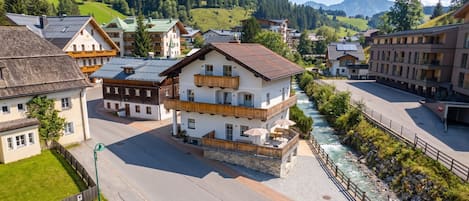 Ein mehrstöckiges Gebäude mit Balkonen, an dessen Seite ein Fluss fließt, mit einem Bergpanorama im Hintergrund.