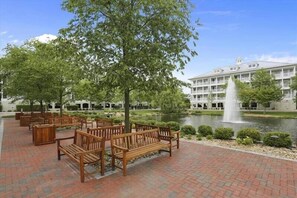 A courtyard with wooden benches, a fountain, and a building with multiple windows in the background. - New 2026! Indoor/Outdoor Pools, Kiddie Pool, Bike path, Interactive Fountains! (Ocean City)