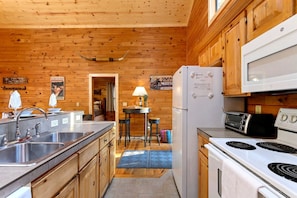 A cabin-style kitchen with wooden walls, a central island, a refrigerator, a microwave, and a stove. - Fully Furnished Cabin with Fire Pit Perfect for Small Groups in Oklahoma (Broken Bow)
