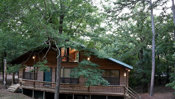 Eine Blockhütte mit einer Terrasse, großen Fenstern und einer Treppe zum Eingang.