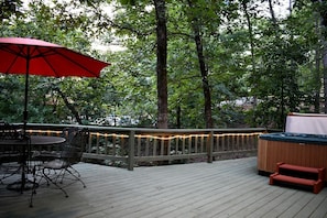 A wooden deck with a hot tub, a table with chairs, and string lights. - Fully Furnished Cabin with Fire Pit Perfect for Small Groups in Oklahoma (Broken Bow)