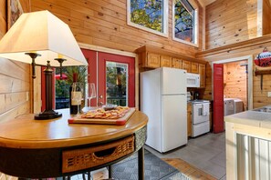 A kitchen with wooden cabinets, a refrigerator, a microwave, and a dining table with a lamp and a fruit platter. - Fully Furnished Cabin with Fire Pit Perfect for Small Groups in Oklahoma (Broken Bow)