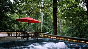 Ein Whirlpool, umgeben von einer Terrasse mit einem roten Sonnenschirm und Bäumen.