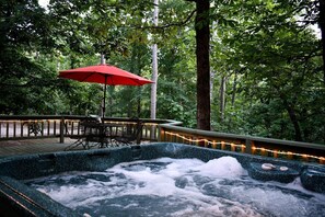 A hot tub surrounded by a deck with a red umbrella, surrounded by trees. - Fully Furnished Cabin with Fire Pit Perfect for Small Groups in Oklahoma (Broken Bow)