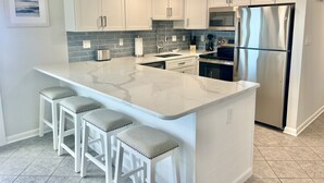 Une cuisine moderne avec des meubles blancs, un îlot en marbre, des appareils électroménagers en acier inoxydable et un pare-feu bleu.