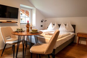 A bedroom with a bed, a TV mounted on the wall, a dining table with chairs, and a window. - Apartments VALI Hochkönig - TOP 4, Ski In/Out (Dienten am Hochkönig)