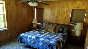 Une chambre à coucher avec un lit, un ventilateur de plafond, des murs en bois, une fenêtre et une table de chevet avec une lampe.