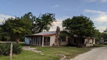 A rustic building with a large tree in front, a small shed, and a dirt path.