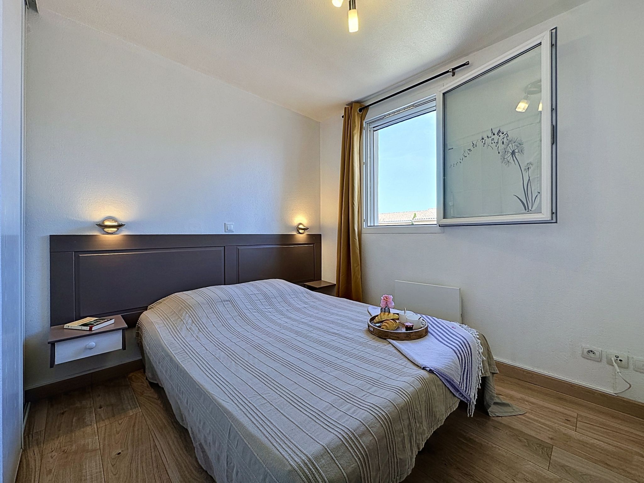 A hotel room with a bed, bedside tables, a window with curtains, and a wall-mounted artwork.