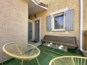 A patio with a bench, two wicker chairs, and a table with cups and saucers. - Mas des Vignes - La Pimprenelle by Interhome (Calvisson)