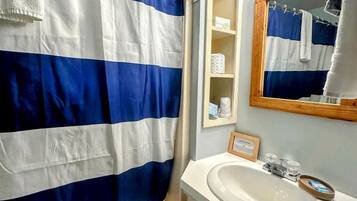 A bathroom with a shower curtain, a sink, a mirror, and a shelf with toiletries.