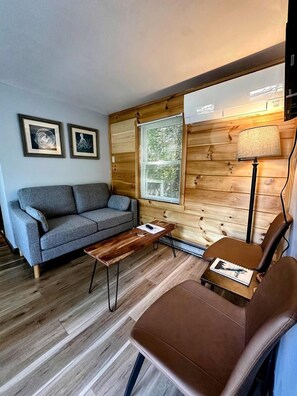 A cozy room with a grey sofa, a wooden coffee table, a brown leather chair, and a lamp.