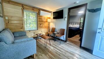 A compact living area with a sofa, two chairs, a small table, a TV mounted on the wall, and a wooden floor.