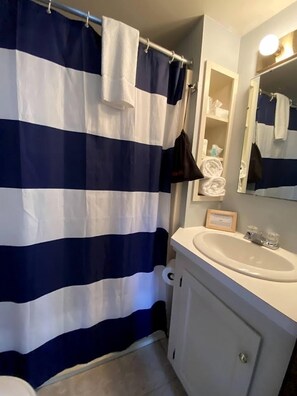 A bathroom with a striped shower curtain, a sink, a mirror, and a towel rack. - Cozy Maine Cottage with Outdoor Dining & Modern Comforts near Camden (Lincolnville)
