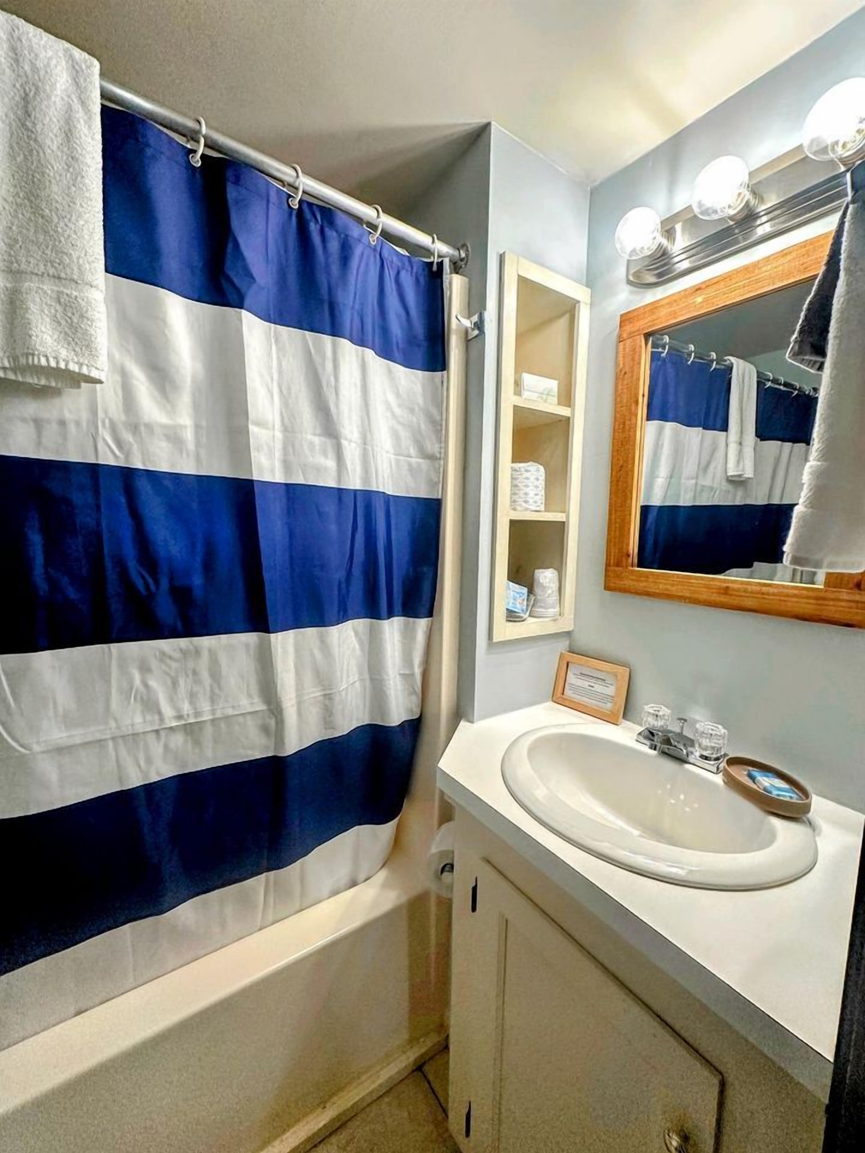 A bathroom with a shower curtain, a sink, a mirror, and a shelf with toiletries.