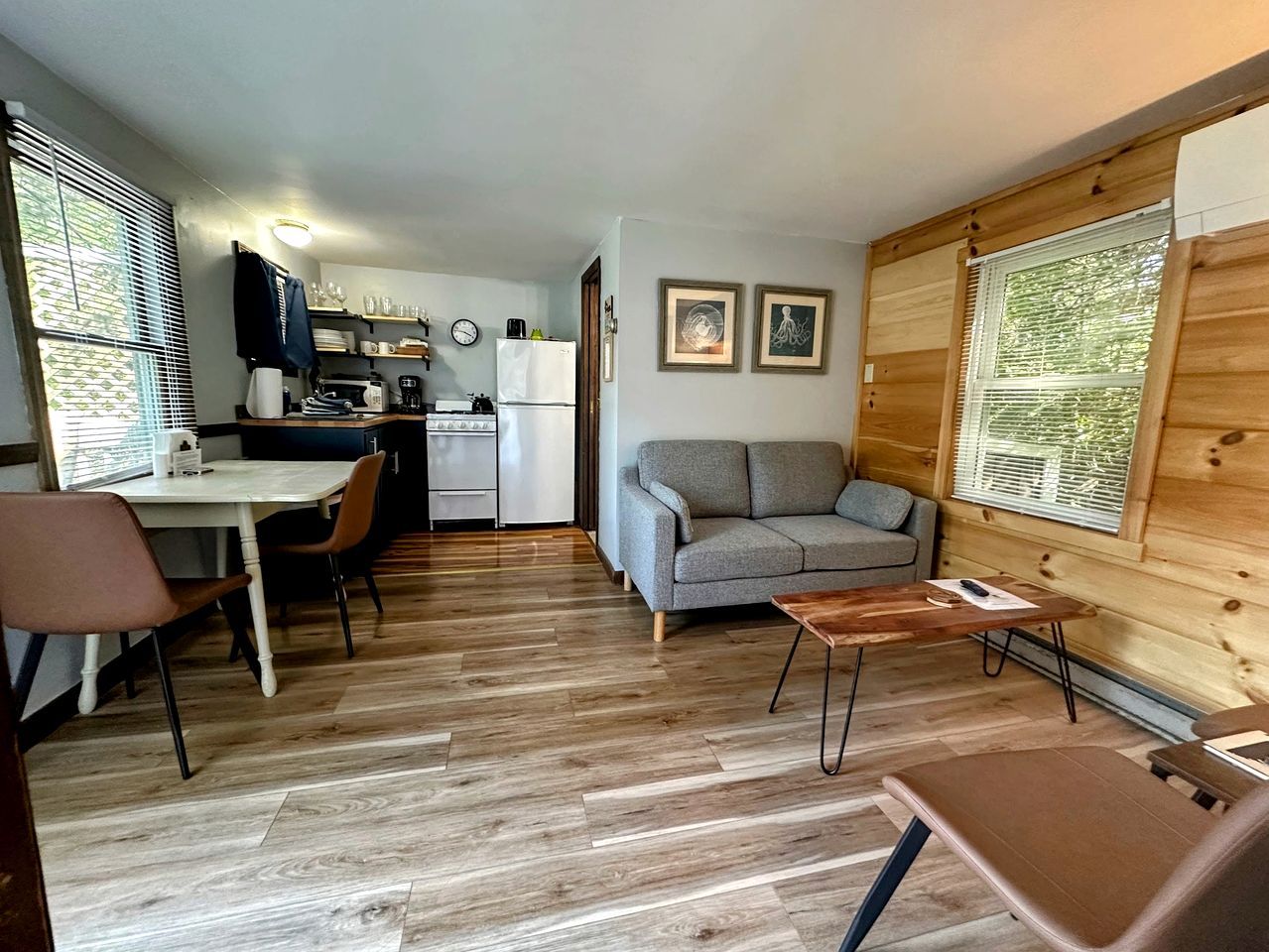 Un espacio habitable compacto con kitchenette, un sofá, una mesa de comedor y piso de madera.