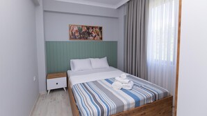Ein Schlafzimmer mit einem Bett, einem Nachttisch, einem Gemälde und einem Fenster mit Vorhängen.