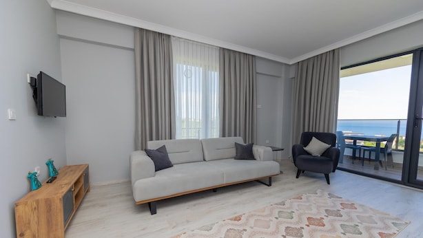 Ein modernes Wohnzimmer mit Sofa, Sessel, Fernseher und Meerblick vom Balkon.
