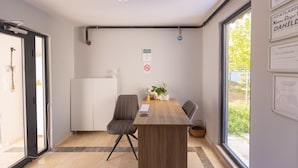 Ein modernes Zimmer mit Holztisch, zwei Stühlen, einem weißen Heizkörper und einem Fenster mit Blick auf Grünflächen.