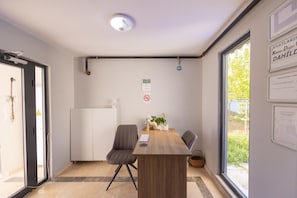 A modern room with a wooden table, two chairs, a white radiator, and a window with a view of greenery. - SİNORA APART (MERKEZ)