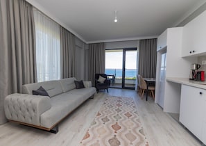A modern living room with a sofa, a dining area, and a kitchen. - SİNORA APART (MERKEZ)