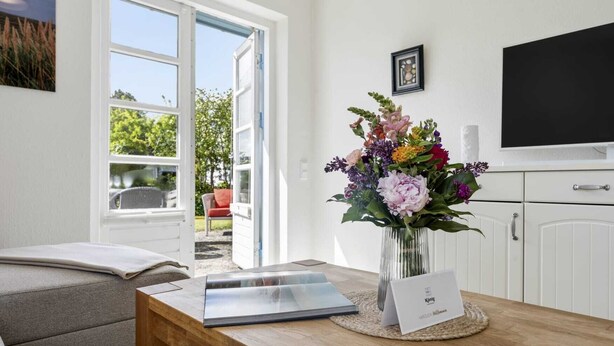 Ett rum med ett träbord, en bärbar dator, en vas med blommor, en inramad tavla och en tv på väggen.