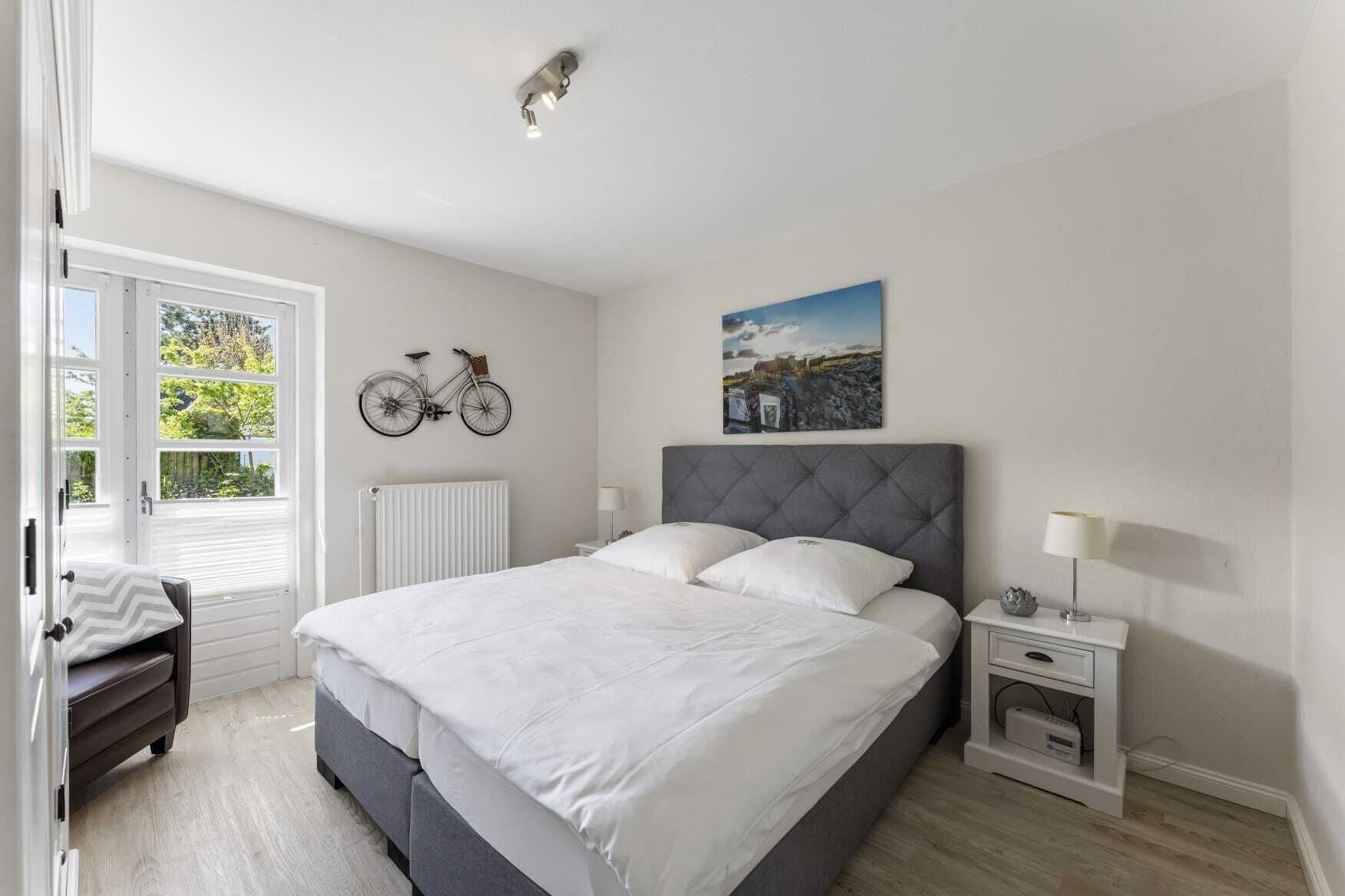 Et soveværelse med en seng, et natbord, en lampe, cykelkunst på væggen, en radiator og et vindue med udsigt.
