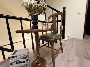 Una silla de madera con un cojín verde, un jarrón con flores, y una mesa con libros y una caja.