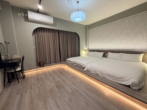 Quarto de hotel moderno com piso de madeira curvado, uma escrivaninha com abajur, cama com roupa de cama branca e luminária no teto.
