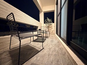 Uma área de estar externa com um banco e mesa, um vaso de planta e vista do céu noturno.