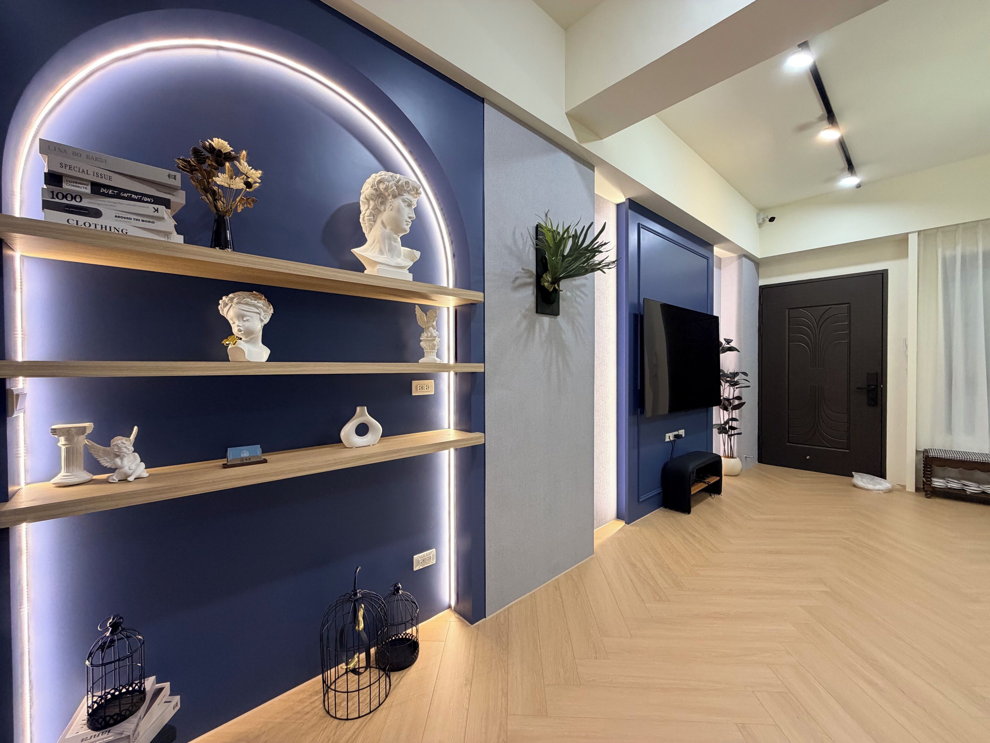 Una sala de estar moderna con una pared azul de acento, estanterías de madera, un televisor de pantalla plana y una puerta negra.