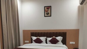 A hotel room with a bed, a nightstand, an air conditioning unit, and a painting on the wall.